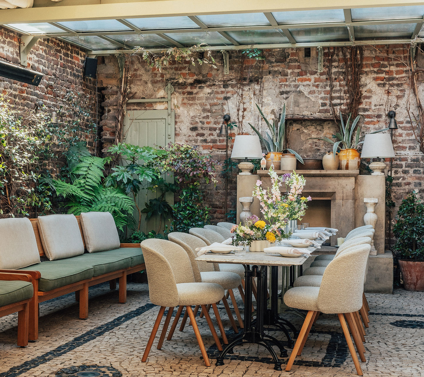 Blick auf zwei Schreibtische mit üblichen Büromaterialien, und grünen Akustikelementen. Im Vordergrund rechts und seitlich links je eine Zimmerpflanze. Hinten ein raumhoher Raumteiler mit schwarzen, vertikalen Lamellen.