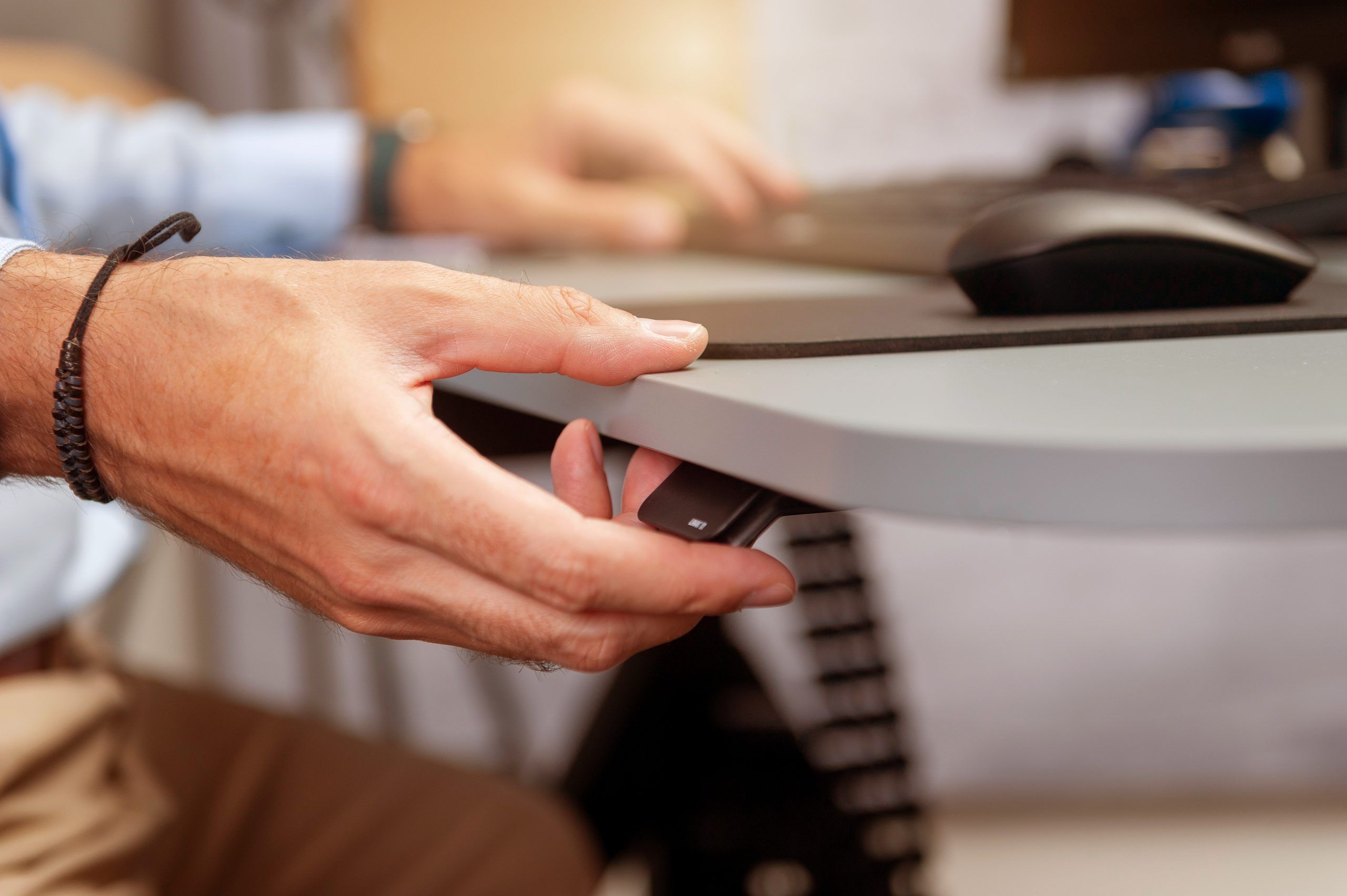Hand greift nach Bedienelement eines höhenverstellbaren Schreibtisches.
